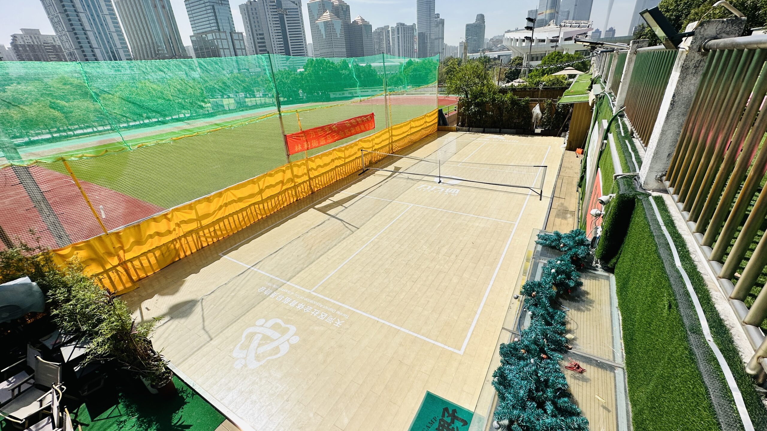 Outdoor sports court with interlocking plastic floor tiles and safety netting next to tall city buildings